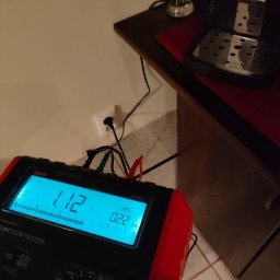 ElectricLoop - Miernik elektryczny UT593 z podłączonymi przewodami do gniazdka elektrycznego, wskazujący wartości pomiarowe na wyświetlaczu. Obok ekspres do kawy.