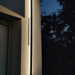 ElectricLoop - Nowoczesne oświetlenie elewacyjne LED w Bydgoszczy, zintegrowane z kamerą monitoringu. Dwa pionowe panele świetlne na teksturowanej ścianie budynku.