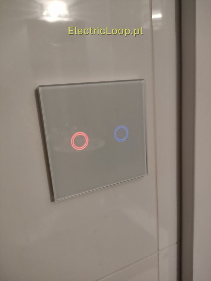 Szklany, dotykowy włącznik światła z podświetleniem LED (czerwony i niebieski) zamontowany na kafelkowanej ścianie. Nowoczesny design.