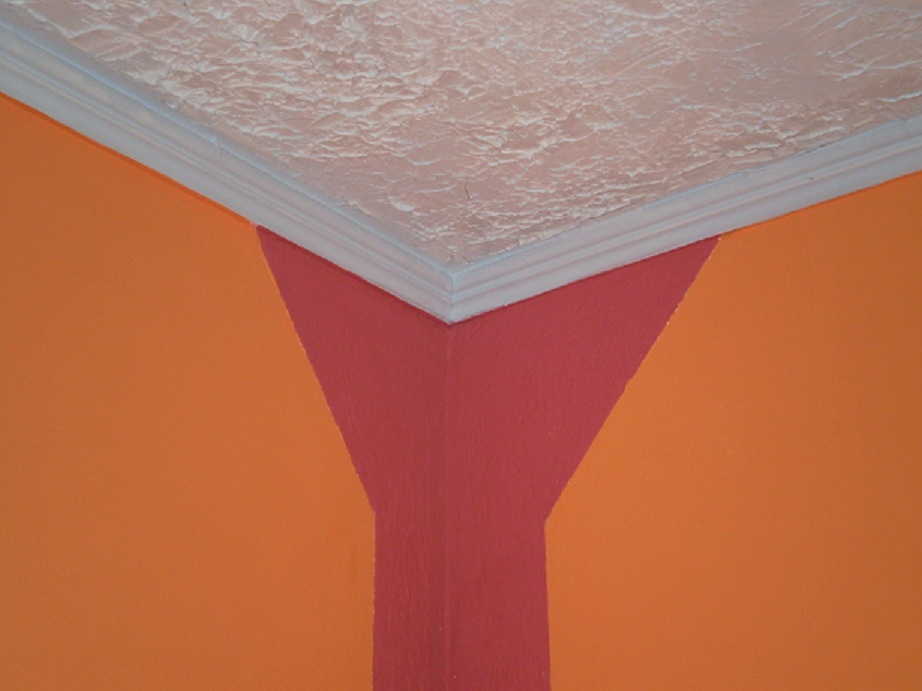Pomarańczowa ściana z narożnikiem pomalowanym na czerwono, biały ozdobny gzyms sufitowy i sufit z teksturą.