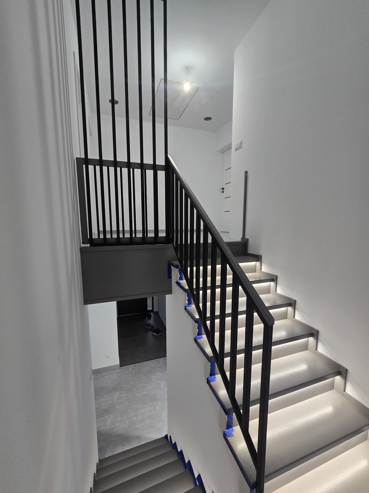 Nowoczesne schody z podświetleniem LED i czarną balustradą, widok z góry. Minimalistyczny design, białe ściany, taśmy zabezpieczające na schodach.