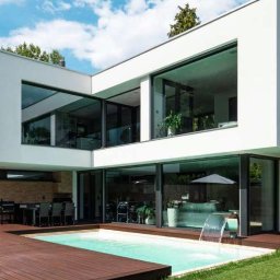 HAPIO GRZEGORZ KOCZERBA - Nowoczesny dom z dużymi oknami aluminiowymi i basenem, minimalistyczna architektura, jasne wnętrza widoczne przez przeszklenia, drewniany taras.