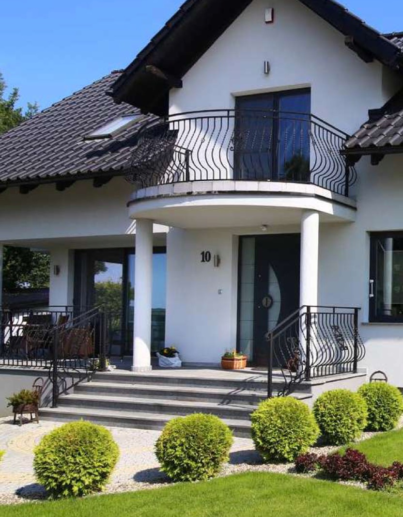 Elegancki dom z balkonem i czarną stolarką okienną, widok z zewnątrz. Schody wejściowe prowadzą do drzwi z numerem 10, otoczone zielenią.