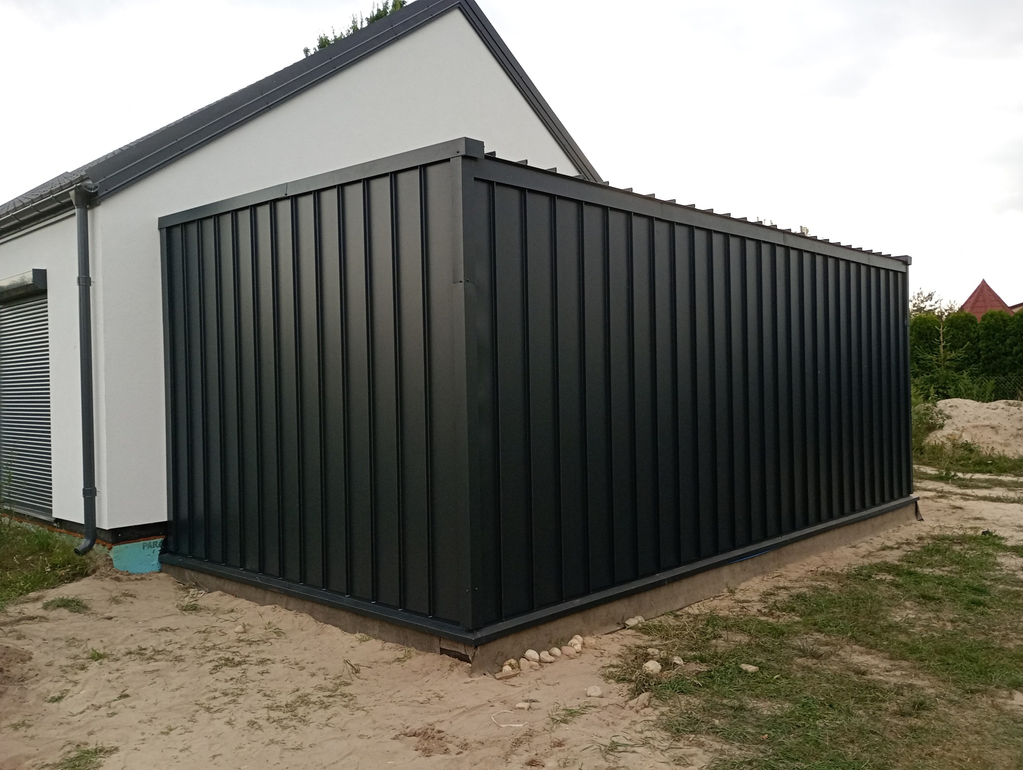 Nowoczesna, grafitowa obróbka blacharska na budynku jednorodzinnym z białym tynkiem. Widoczne pionowe panele i staranne wykończenie narożników.