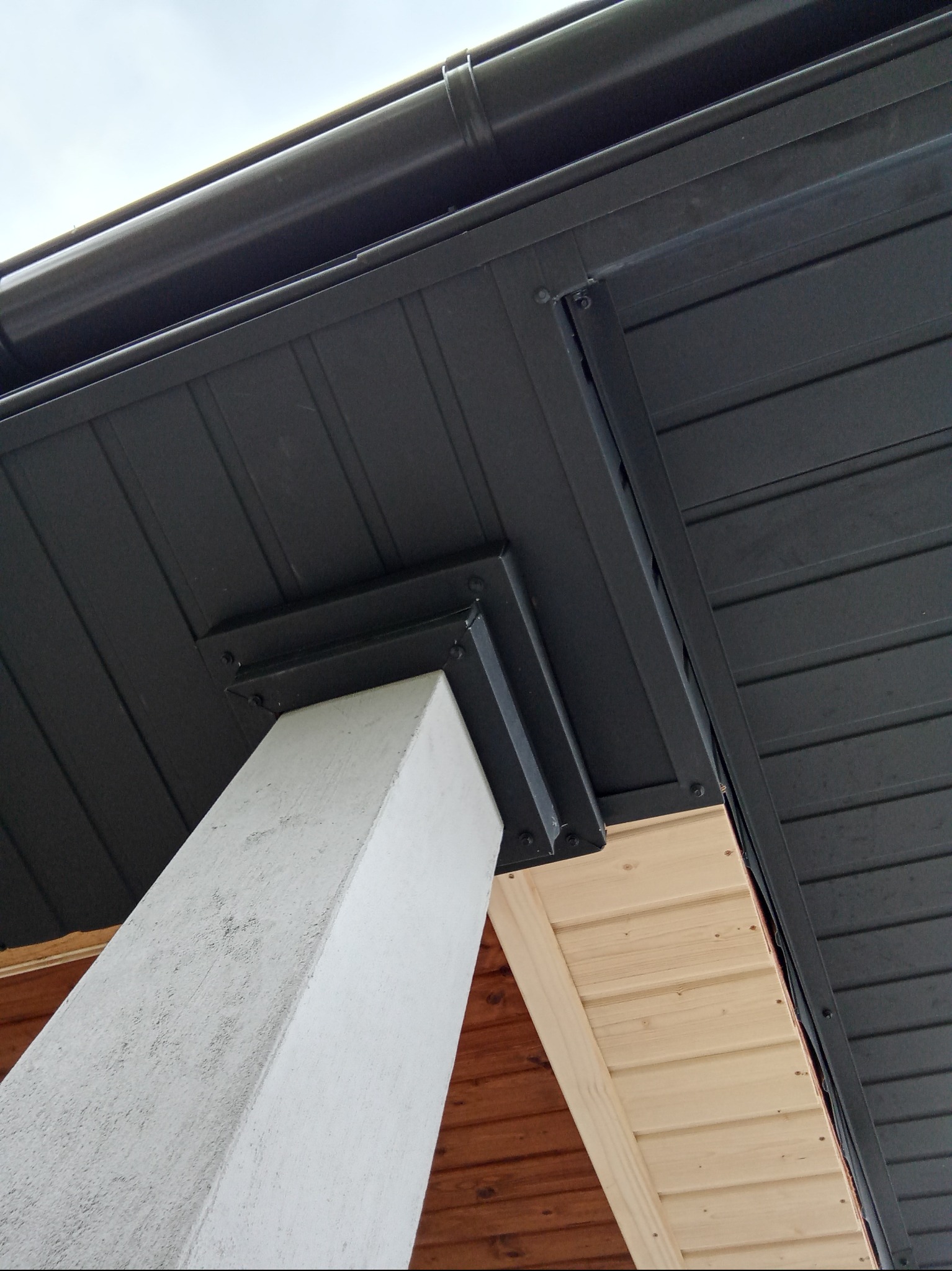 Detal zadaszenia: ciemna podbitka z rynną, wsparta na białym słupie. Widoczne drewniane elementy konstrukcji. Ujęcie z dołu, podkreślające solidność wykonania.