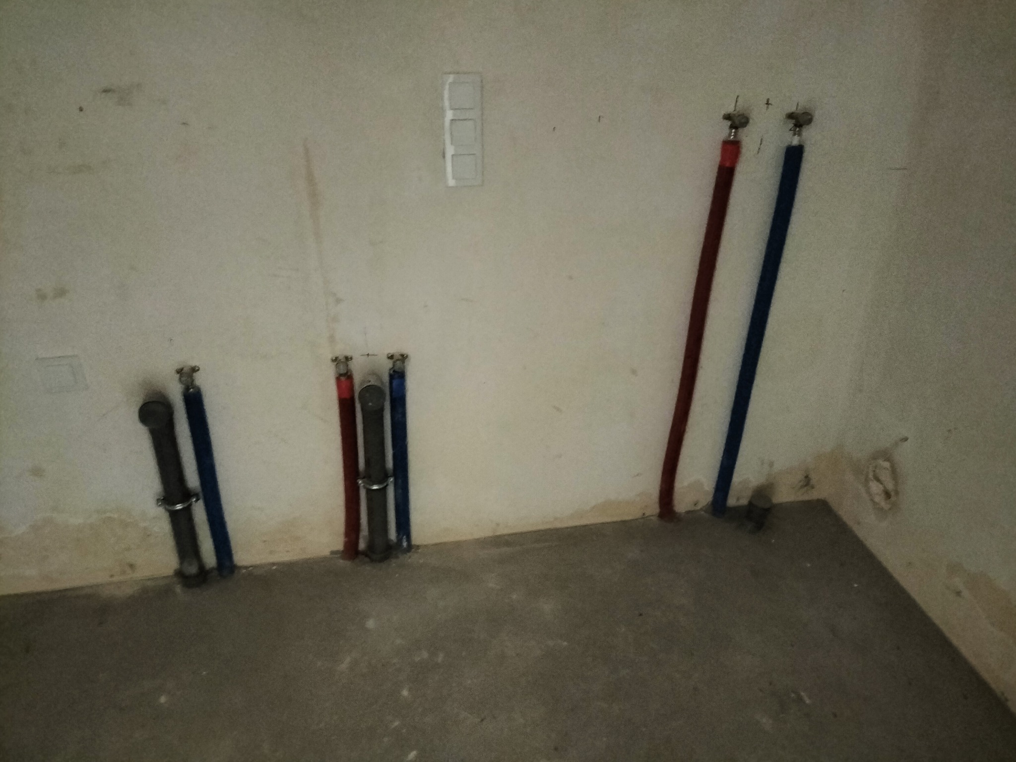 Instalacja wodna z rurami PEX w kolorze czerwonym i niebieskim, wyprowadzone ze ściany w nowym budynku w Poznaniu. Widoczne przyłącza i fragment surowej ściany.
