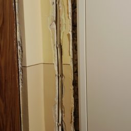 Wikadem Usługi Elektryczne Marcin Jarzyński - Przewody elektryczne w ścianie przed tynkowaniem w Płocku. Widoczne kable zabezpieczone uchwytami, ściana w trakcie prac remontowych.