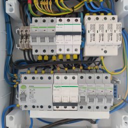 Wikadem Usługi Elektryczne Marcin Jarzyński - Rozdzielnica elektryczna z bezpiecznikami, przewodami oznaczonymi numerami i listwami zaciskowymi w kolorach zielonym i niebieskim. Widok z góry na wnętrze skrzynki.