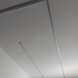Wikadem Usługi Elektryczne Marcin Jarzyński - Minimalistyczne oświetlenie sufitowe LED z cienkimi, prostokątnymi profilami, tworzące nowoczesny wzór na białym suficie. Delikatne światło podkreśla geometrię.