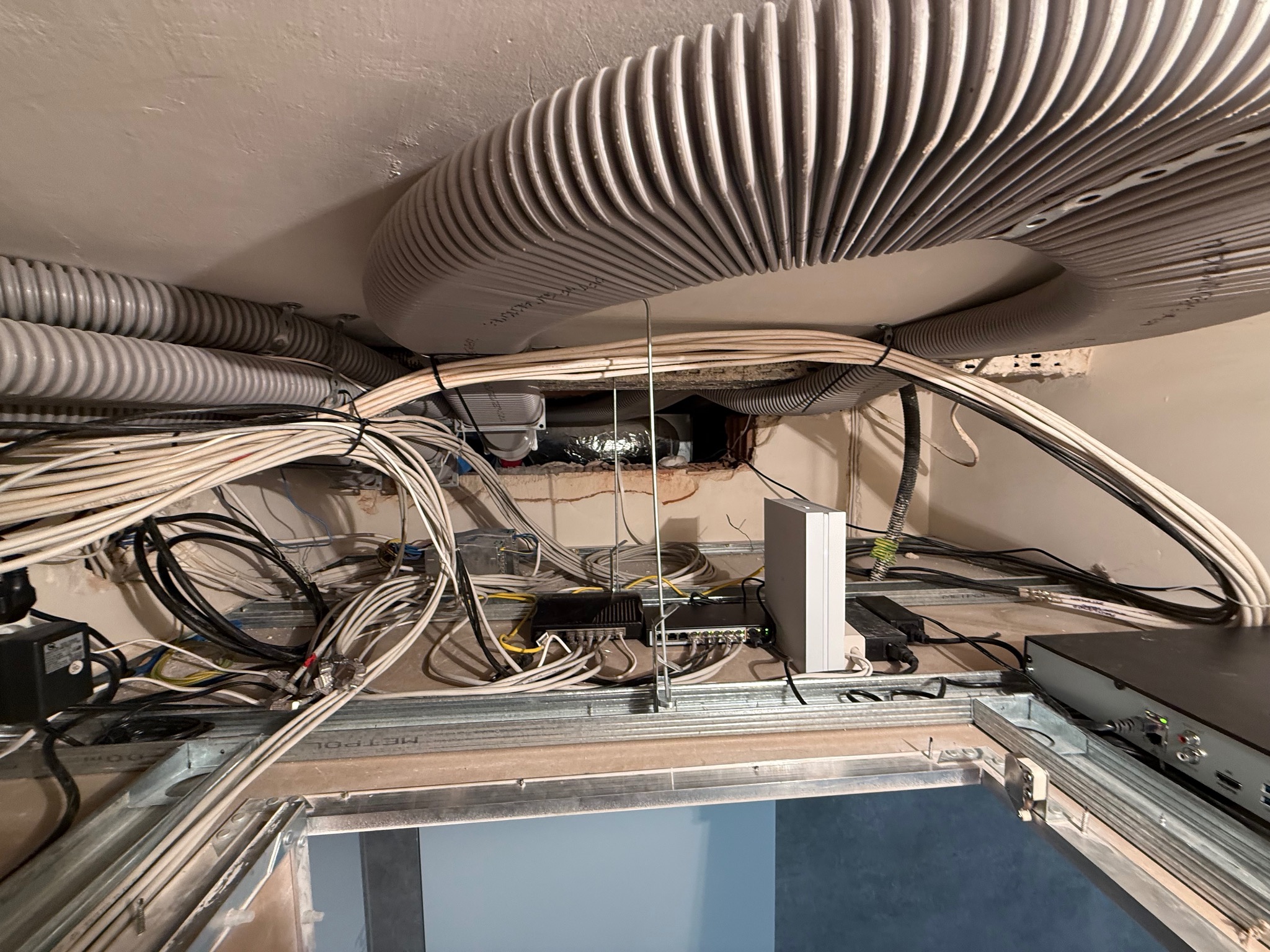 Sufit podwieszany w trakcie montażu z widocznymi kablami, rurami wentylacyjnymi i urządzeniami sieciowymi. Metalowa konstrukcja sufitu.