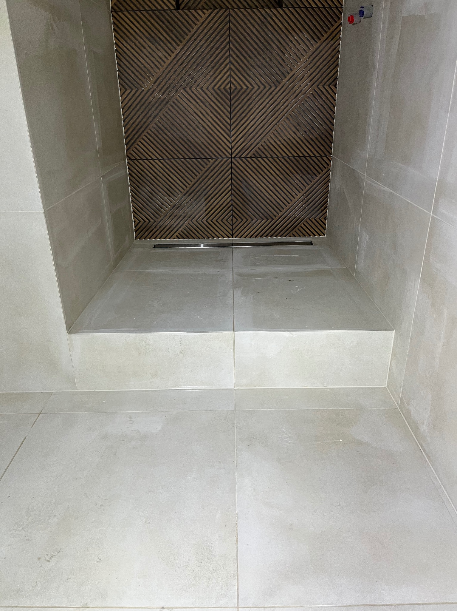 Wykończona kabina prysznicowa z odpływem liniowym i dekoracyjną, drewnopodobną okładziną ścienną. Jasne płytki podłogowe i ścienne tworzą spójną całość.