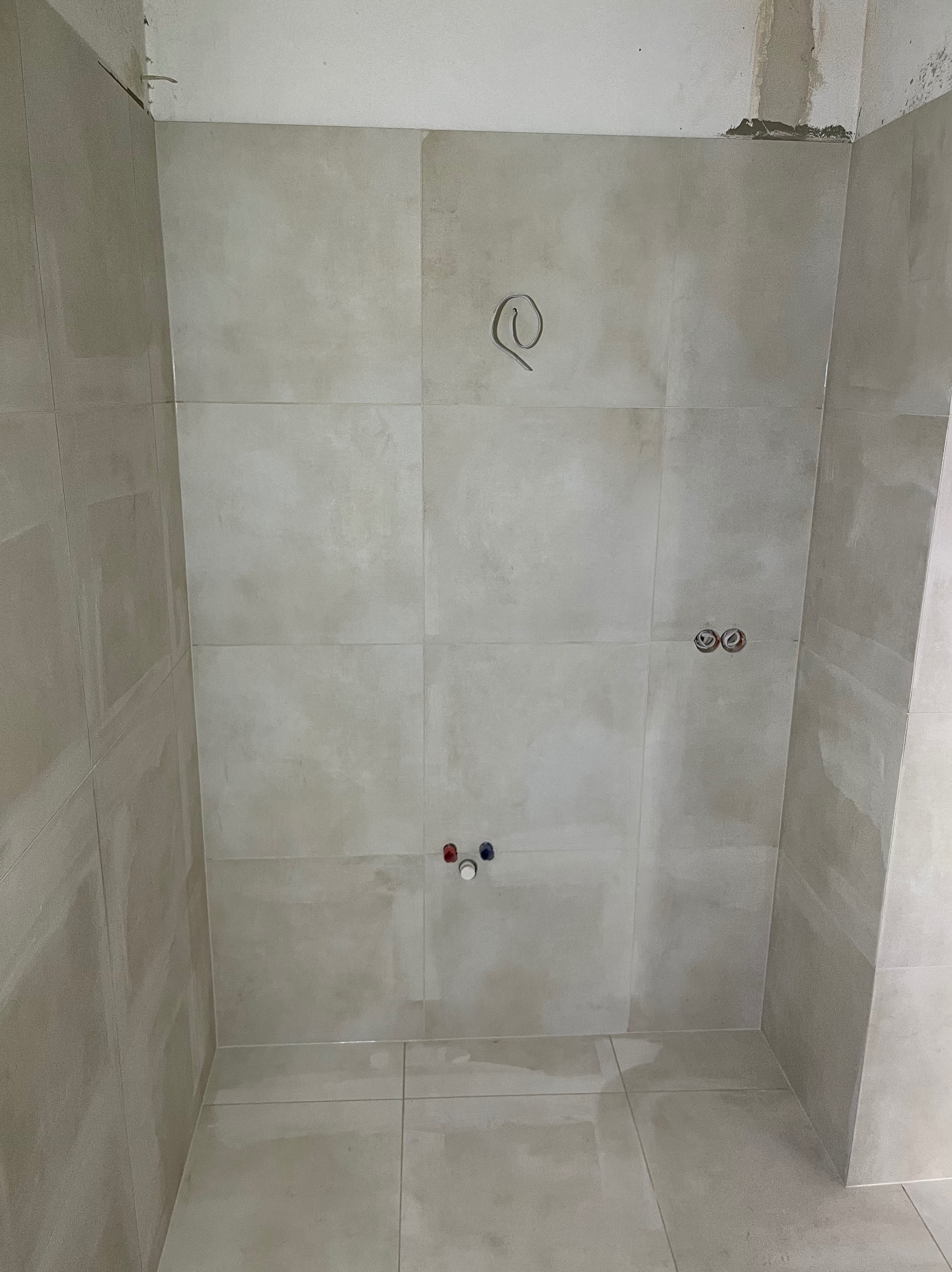 Wykończona łazienka z beżowymi płytkami, widoczne przyłącza wodne i wyprowadzony kabel elektryczny. Minimalistyczny design, surowy stan wykończenia.