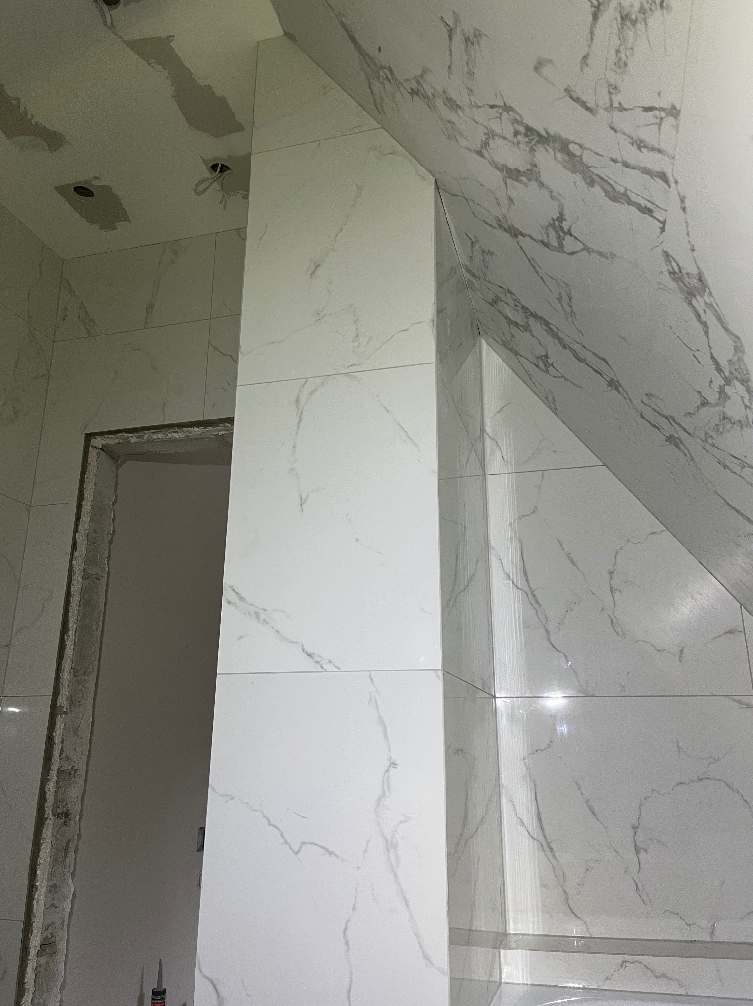 Wykończona ściana i filar w łazience z białych płytek imitujących marmur. Widoczny fragment sufitu i ościeżnica drzwi. Ukośny sufit na poddaszu.