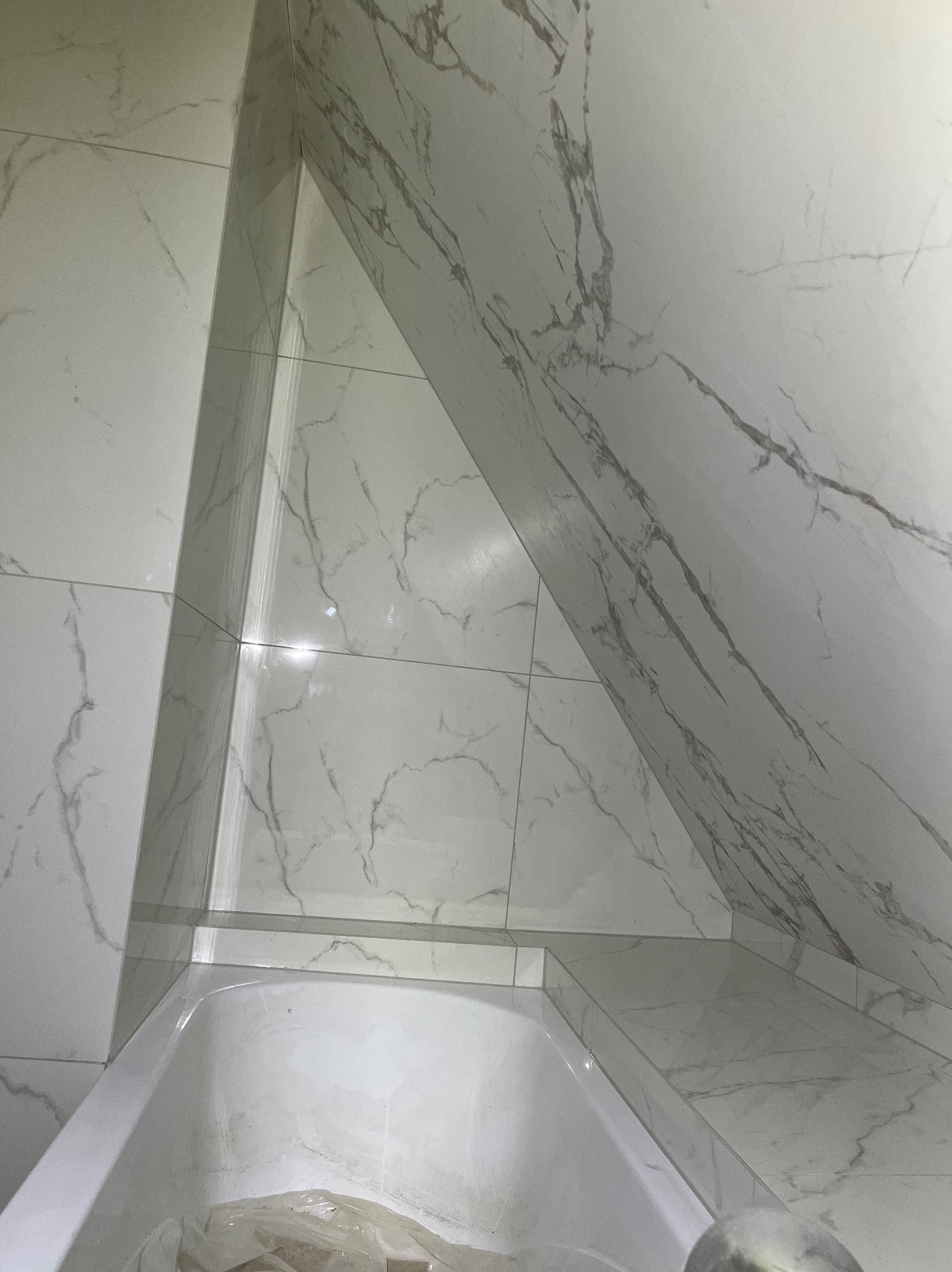 Wykończona łazienka z wanną w zabudowie, wyłożona białymi płytkami imitującymi marmur. Ukośne ściany i precyzyjne fugi podkreślają nowoczesny design.