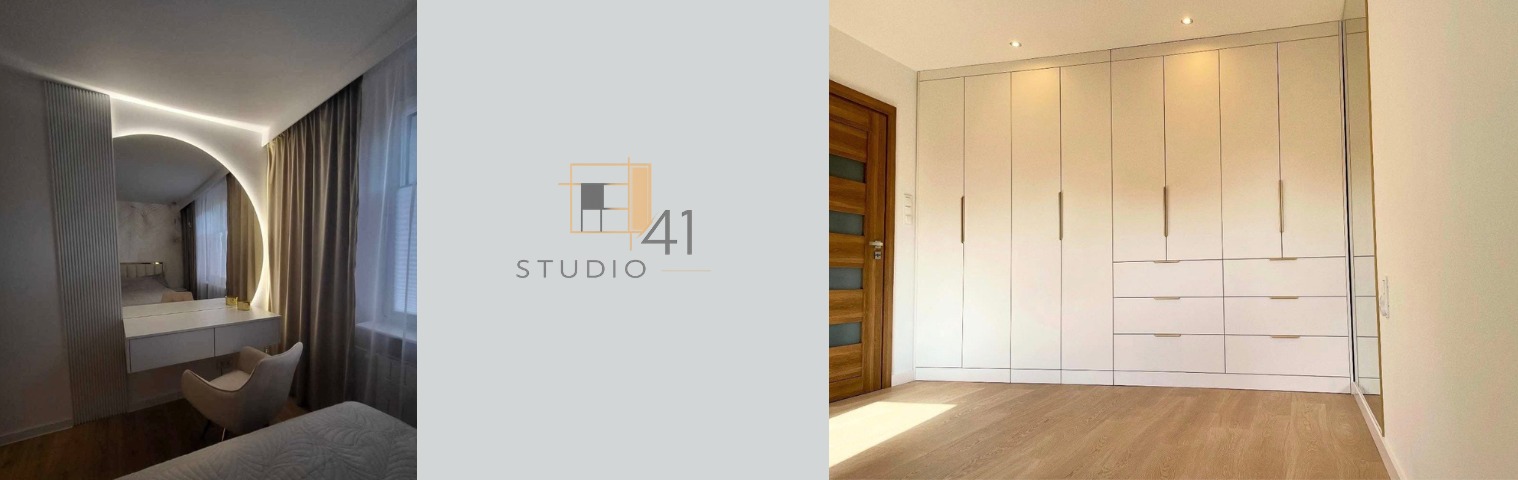 Biała szafa wnękowa z długimi, złotymi uchwytami i komodą, drewniana podłoga, widok z perspektywy pomieszczenia, obok toaletka z okrągłym lustrem z podświetleniem LED.