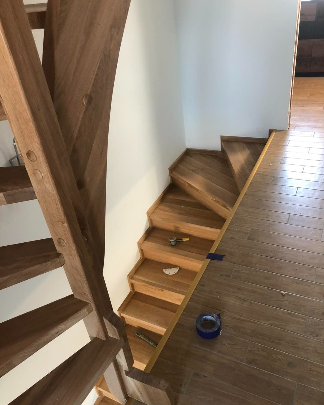 Montaż drewnianych schodów z widocznymi narzędziami i taśmą malarską, ukazujący etap prac wykończeniowych w jasnym wnętrzu.