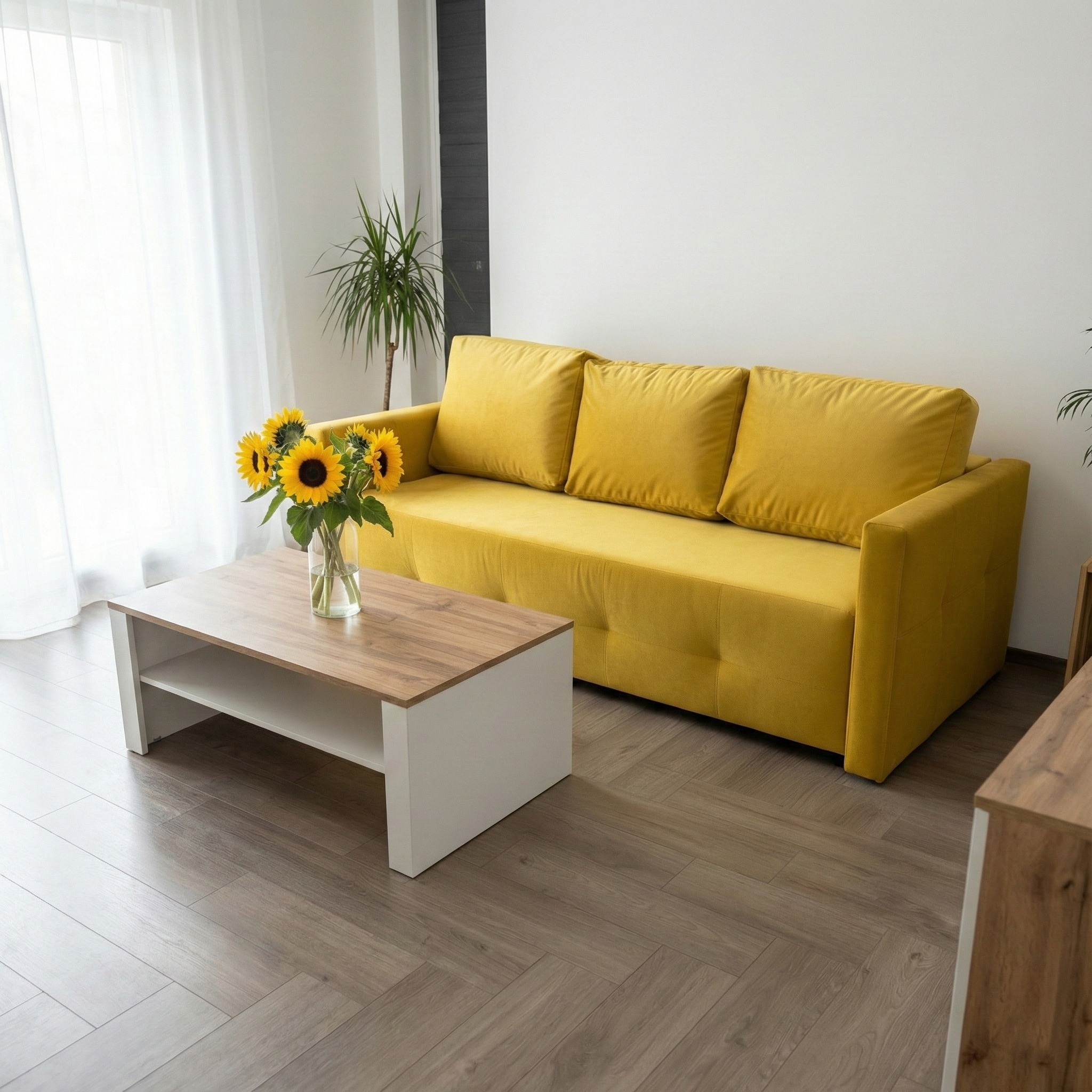 Żółta sofa z poduszkami w jasnym wnętrzu, drewniany stolik kawowy z bukietem słoneczników, parkiet w jodełkę. Minimalistyczny design z akcentem kolorystycznym.
