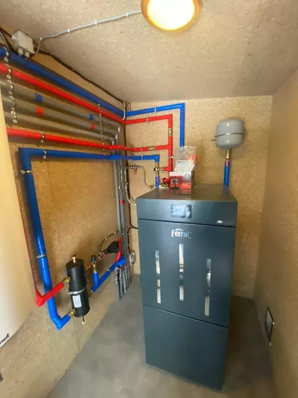 Nowoczesny piec gazowy Ferroli z instalacją CO w pomieszczeniu wyłożonym płytami OSB, widoczne rury w kolorach niebieskim i czerwonym.