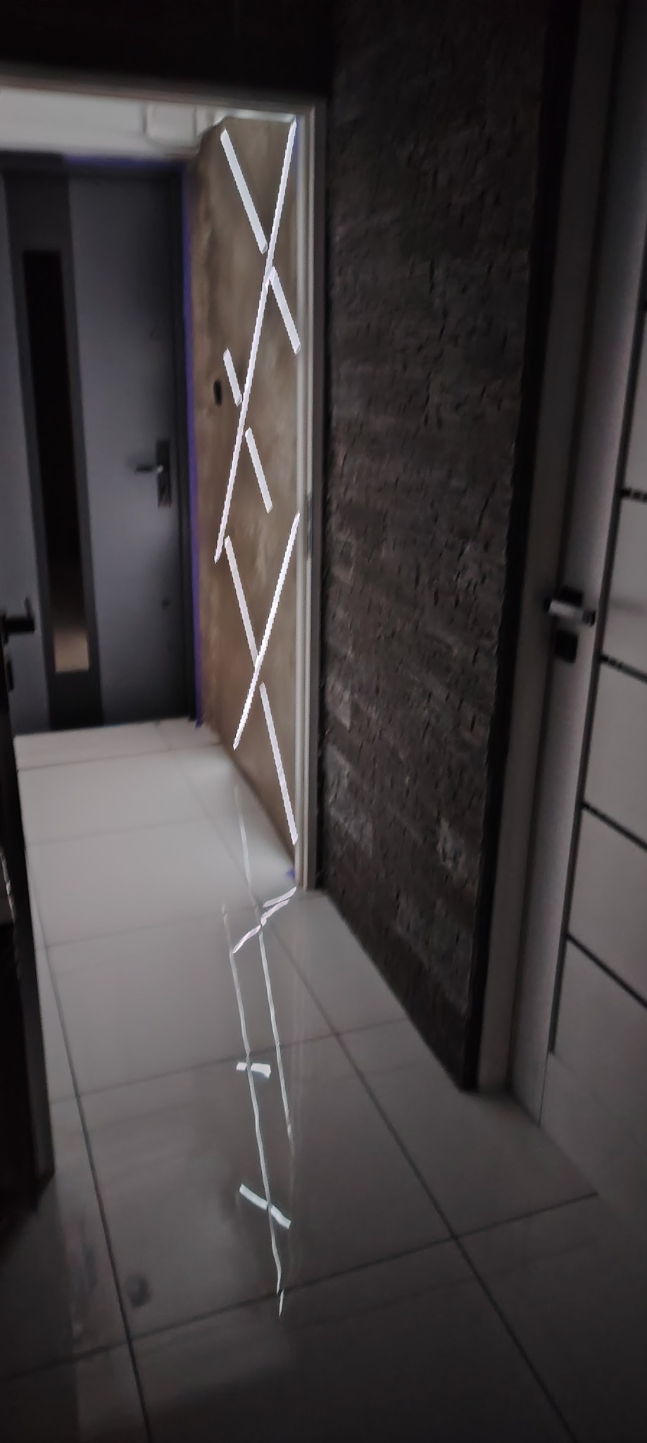 Nowoczesne wykończenie wnętrza: ciemna ściana z fakturą, białe płytki podłogowe z połyskiem i drzwi z geometrycznym wzorem. Widok z perspektywy podłogi.