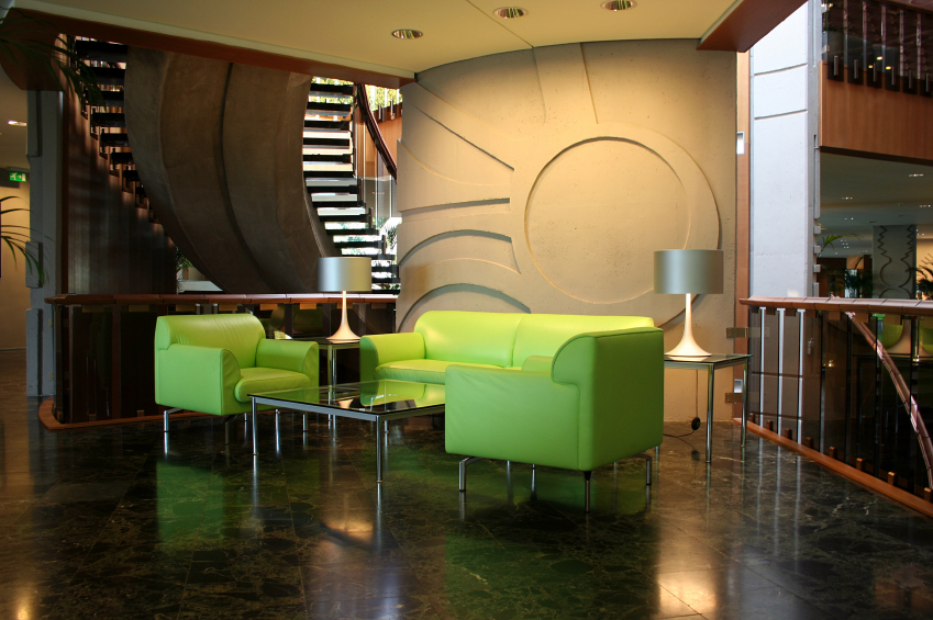 Wnętrze z zielonymi meblami wypoczynkowymi, marmurową podłogą i dekoracyjną ścianą z motywem koła oraz schodami w tle.