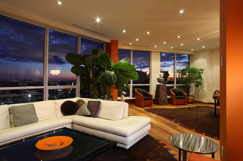 Nowoczesny salon z dużymi oknami, białym narożnikiem, drewnianą podłogą i widokiem na miasto o zmierzchu.