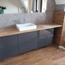 Krzysztof Kozłowski - Nowoczesna łazienka z szarą zabudową pod umywalką, drewnianym blatem i płytkami imitującymi drewno. W lustrze odbija się osoba robiąca zdjęcie.