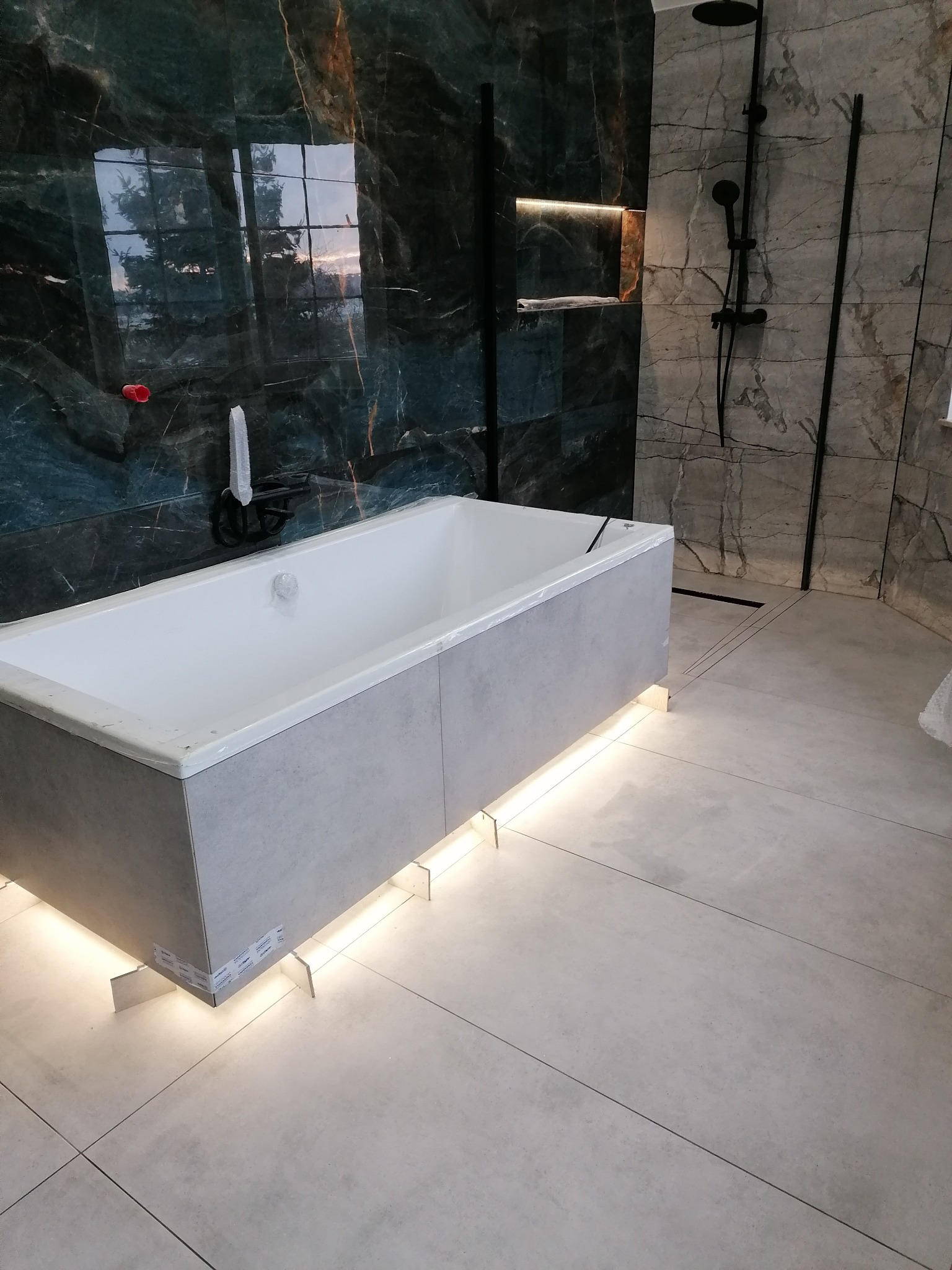 Nowoczesna łazienka z podświetlaną wanną na tle marmurowych płytek i czarnej armatury. Minimalistyczny design z akcentem na oświetlenie.