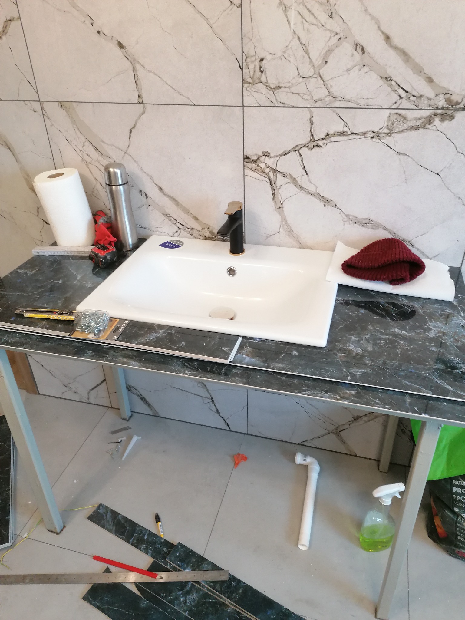 Montaż umywalki nablatowej z czarną armaturą na blacie imitującym marmur, w trakcie prac wykończeniowych łazienki. Widoczne narzędzia i materiały.