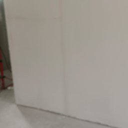 PRZEDSIĘBIORSTWO BUDOWLANE NATKA SPÓŁKA Z OGRANICZONĄ ODPOWIEDZIALNOŚCIĄ - Ściana po szpachlowaniu i malowaniu na gładko, widoczne narzędzia i materiały budowlane w tle. Oświetlenie budowlane. Prace wykończeniowe w trakcie.