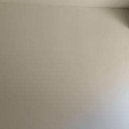 PRZEDSIĘBIORSTWO BUDOWLANE NATKA SPÓŁKA Z OGRANICZONĄ ODPOWIEDZIALNOŚCIĄ - Gładka, pomalowana na biało ściana w rogu pokoju, z surowym oknem w tle. Widoczne ślady po szpachlowaniu przy oknie.