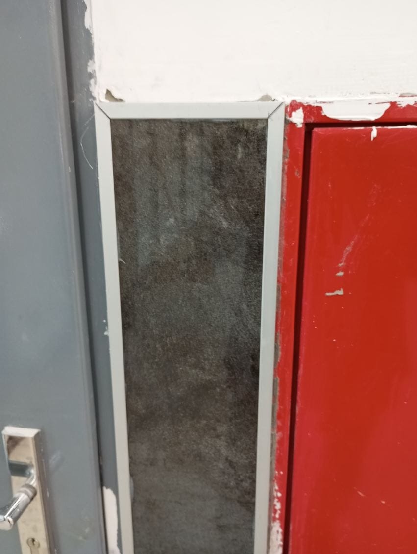 Fragment ściany z widocznym łączeniem płyt kartonowo-gipsowych, szpachlowanych i przygotowanych do malowania, sąsiadujących z drzwiami i szafką.