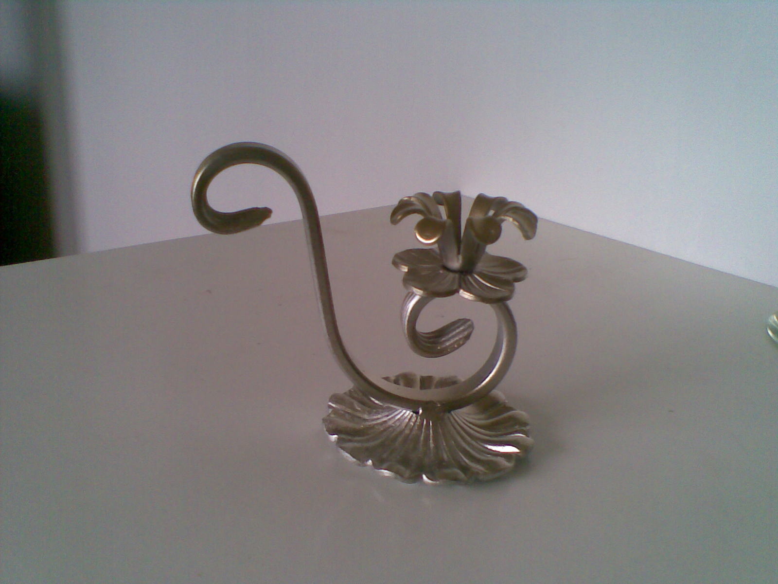 Metalowy, dekoracyjny świecznik z motywem kwiatowym, wykonany z giętego metalu, stojący na białym blacie.