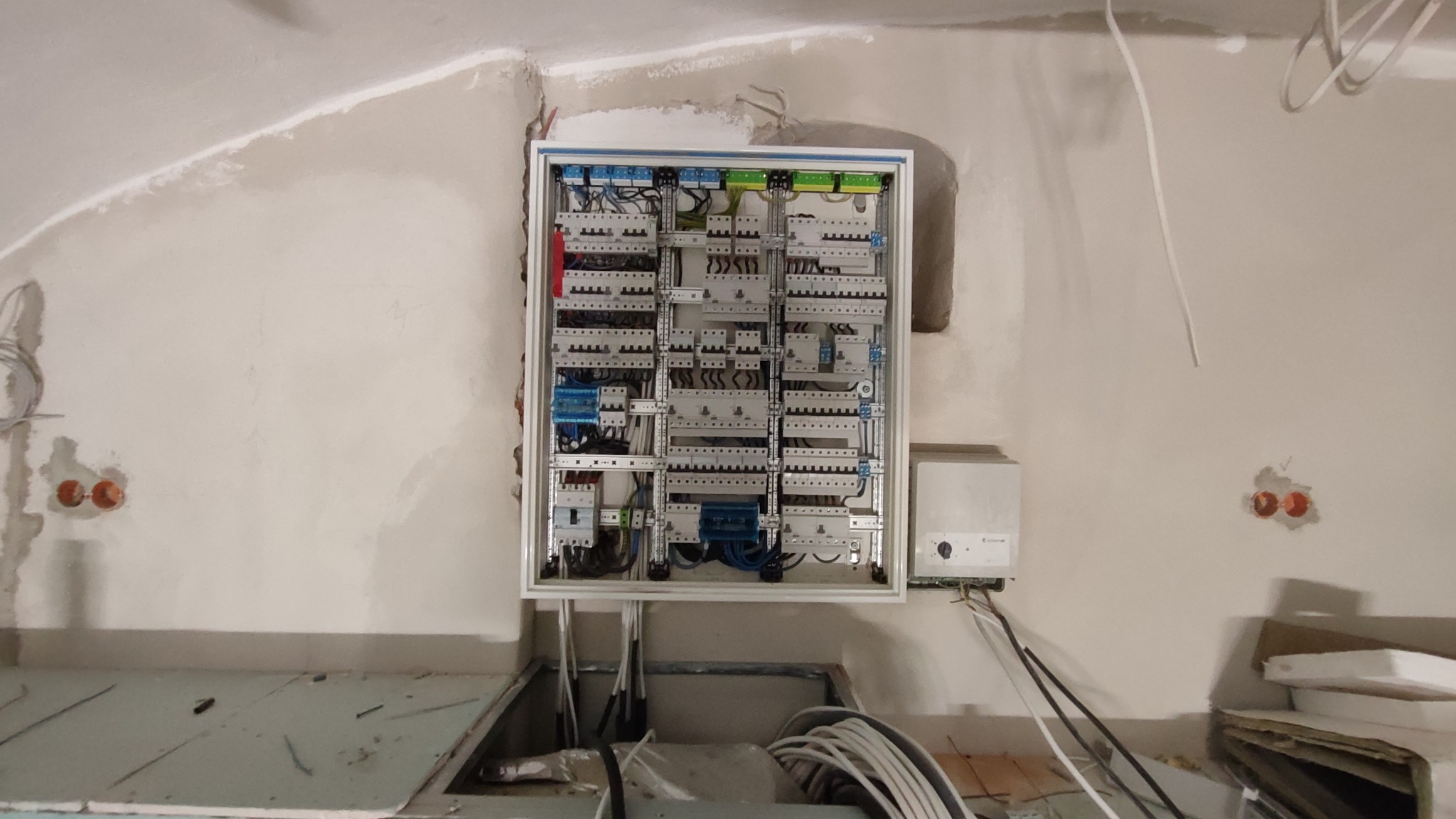 Rozdzielnia elektryczna w trakcie montażu na ścianie w surowym wnętrzu. Widoczne przewody i elementy instalacji. Ściana w stanie deweloperskim.