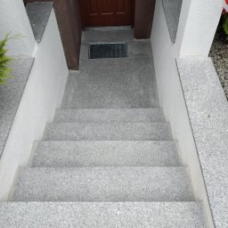 Bogdan Łosiński - Granitowe schody wejściowe z brązowymi drzwiami w tle, wykończone białymi elementami. Widok z góry na szare stopnie i białe ściany.