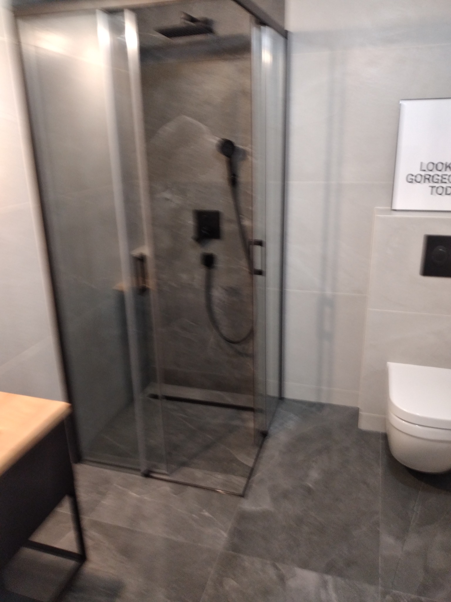 Nowoczesna kabina prysznicowa z czarną armaturą i szarymi płytkami w wykończonej łazience. Minimalistyczny design z akcentem na detale.