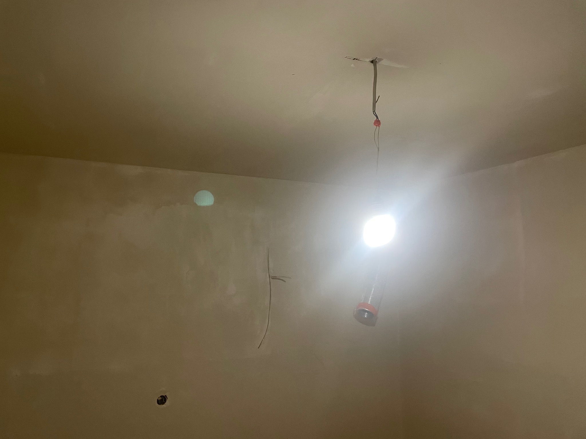 Wnętrze w trakcie szpachlowania: gładkie ściany w beżowym odcieniu, widoczne ślady po szpachli, wiszące przewody oświetleniowe. Przygotowanie do malowania.