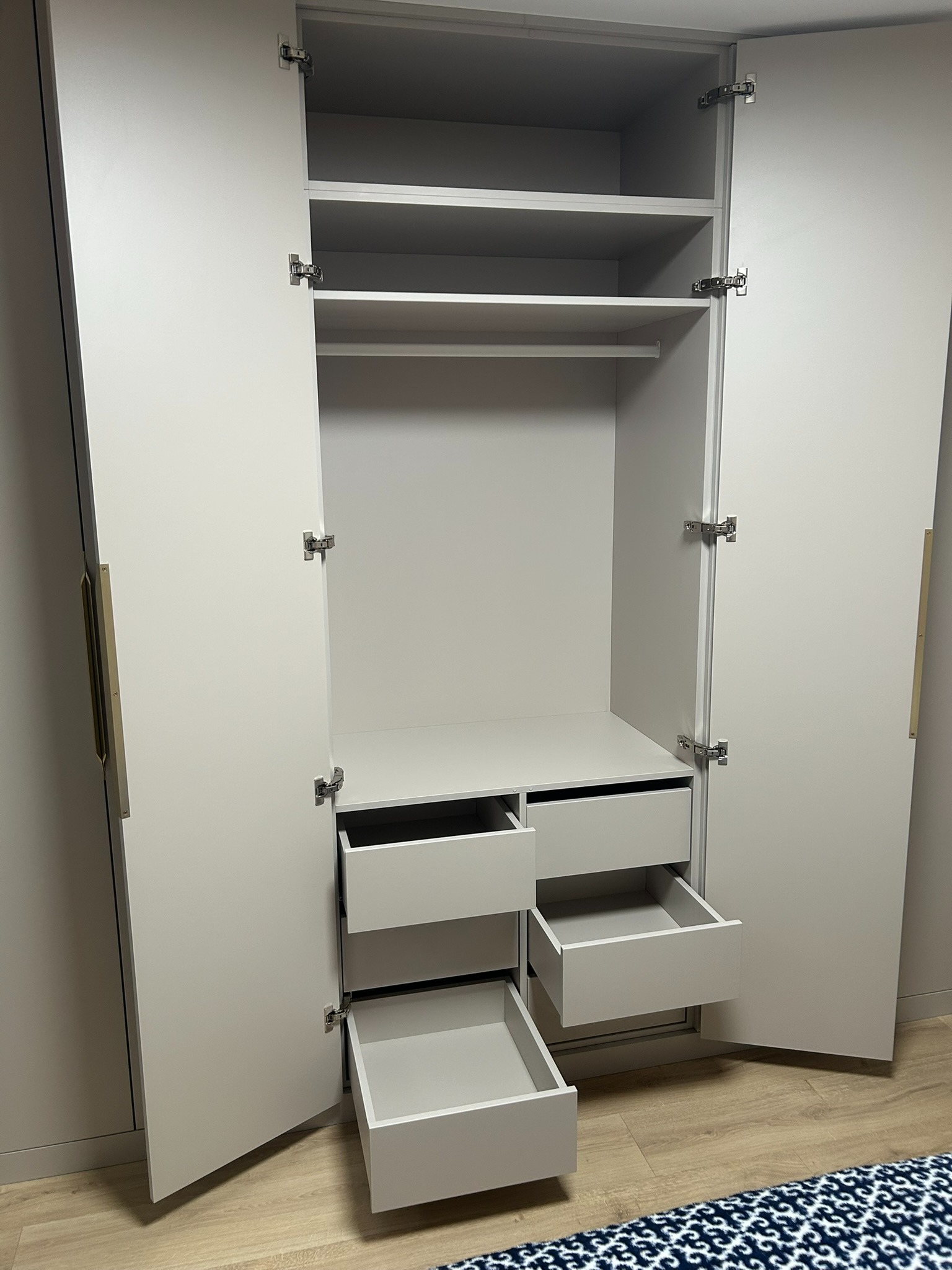 Jasnoszara szafa na wymiar z otwartymi drzwiami i wysuniętymi szufladami, widok z przodu, wnętrze szafy z półkami i drążkiem na ubrania.