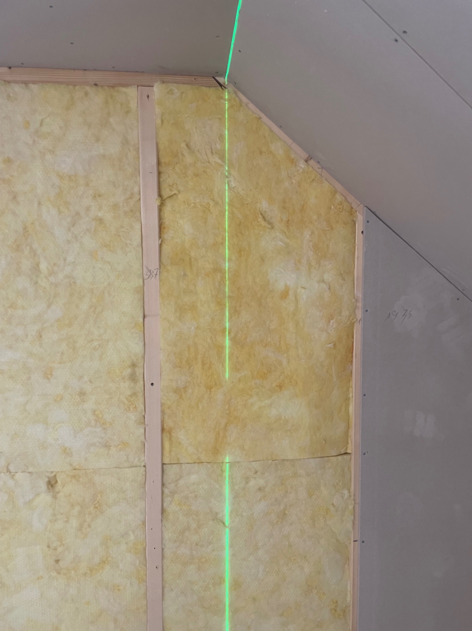 Ocieplenie poddasza wełną mineralną, widoczna konstrukcja drewniana, płyta gipsowo-kartonowa i zielona linia lasera wyznaczająca poziom.