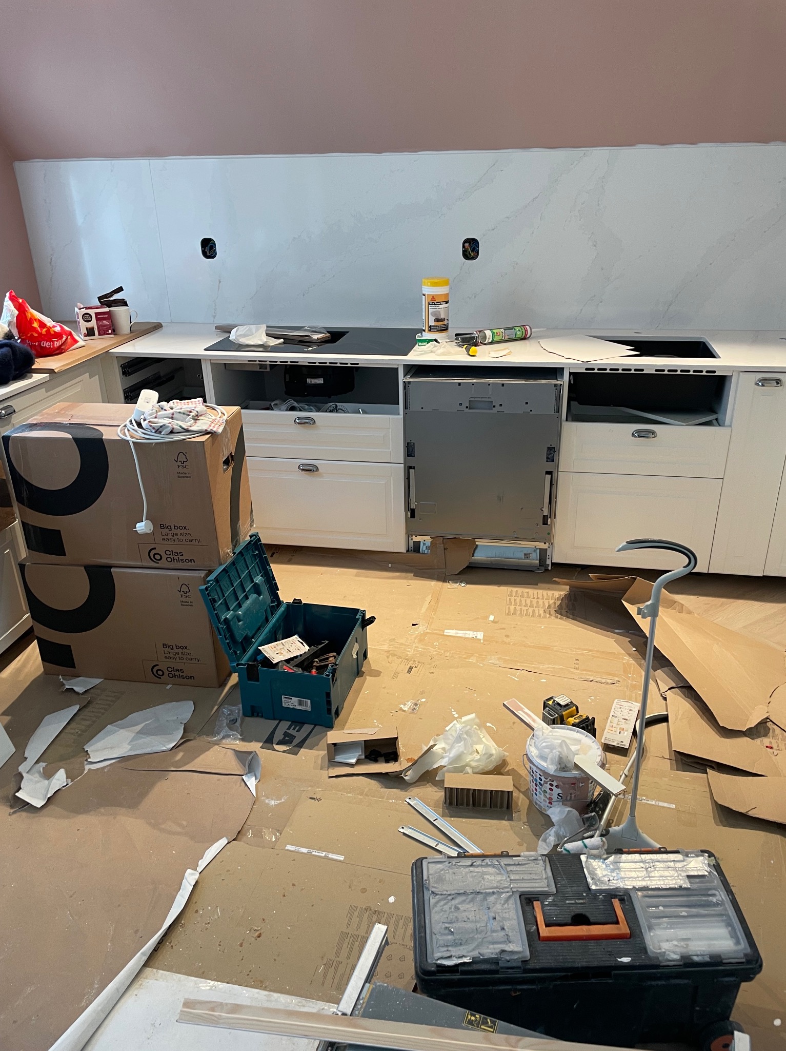 Montaż białych szafek kuchennych z marmurowym blatem, widoczne narzędzia i kartony, etap prac wykończeniowych, wnętrze w trakcie realizacji.