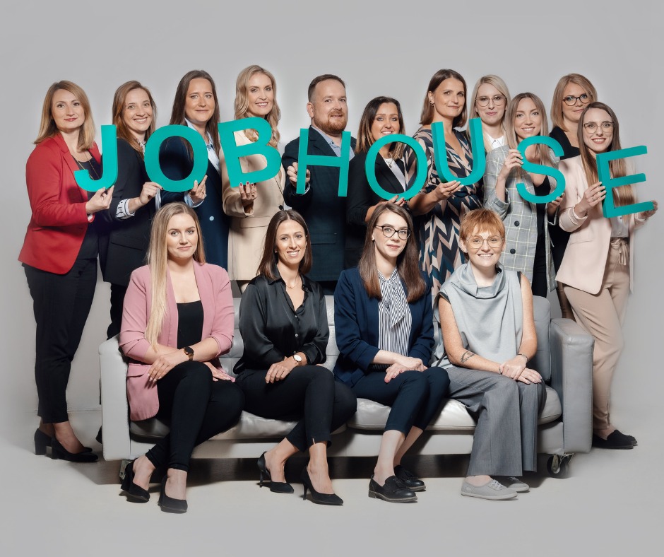 Zespół Jobhouse prezentuje nazwę firmy, trzymając litery na jasnym tle. Uśmiechnięci pracownicy w eleganckich strojach siedzą na sofie i stoją za nią.