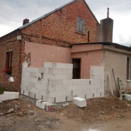 Usługi ogólnobudowlane Sebastian Kocięcki - Budowa domu z czerwonej cegły: wznoszenie ściany z białych bloczków, widoczne narzędzia i gruz. Etap prac murarskich przy dobudowie.