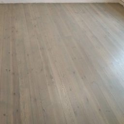 Usługi Ogólnobudowlane - Jasnoszara, odnowiona podłoga z desek, widoczna pod kątem. Świeżo położona, z widoczną strukturą drewna i subtelnymi detalami wykończenia.