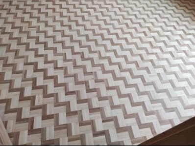 Ułożony parkiet w jodełkę z jasnego i ciemnego drewna, widok z góry, wzór zygzakowaty, równomierne ułożenie, wykończona podłoga, detale łączeń.