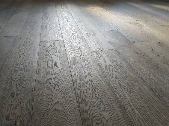 Ułożony parkiet z wyraźnym rysunkiem drewna, wykończony w odcieniach szarości, z delikatnym połyskiem i widocznym naturalnym usłojeniem. Ujęcie pod kątem.