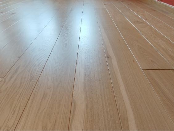 Jasny, lakierowany parkiet ułożony w regularny wzór, widoczny z niskiej perspektywy, podkreślającej strukturę drewna i połyskliwość powierzchni.