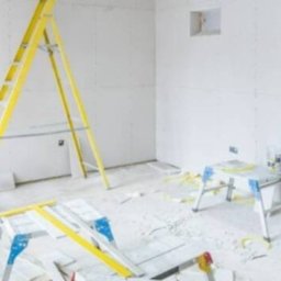 Fachowe ręce - Wnętrze w trakcie prac wykończeniowych: ściany pokryte płytami gipsowo-kartonowymi, żółta drabina oparta o ścianę, widoczne narzędzia i materiały budowlane.