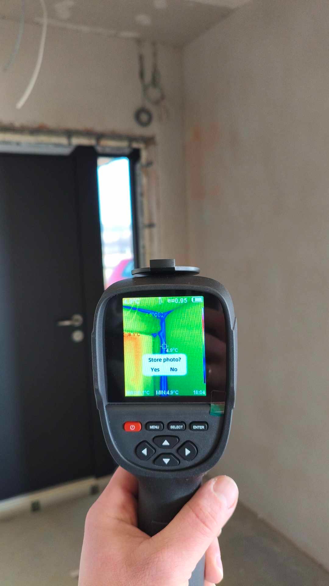 Termowizja w trakcie pomiaru temperatury instalacji w nowym budynku. Na ekranie urządzenia widoczny rozkład temperatur. W tle widoczne przewody instalacyjne.