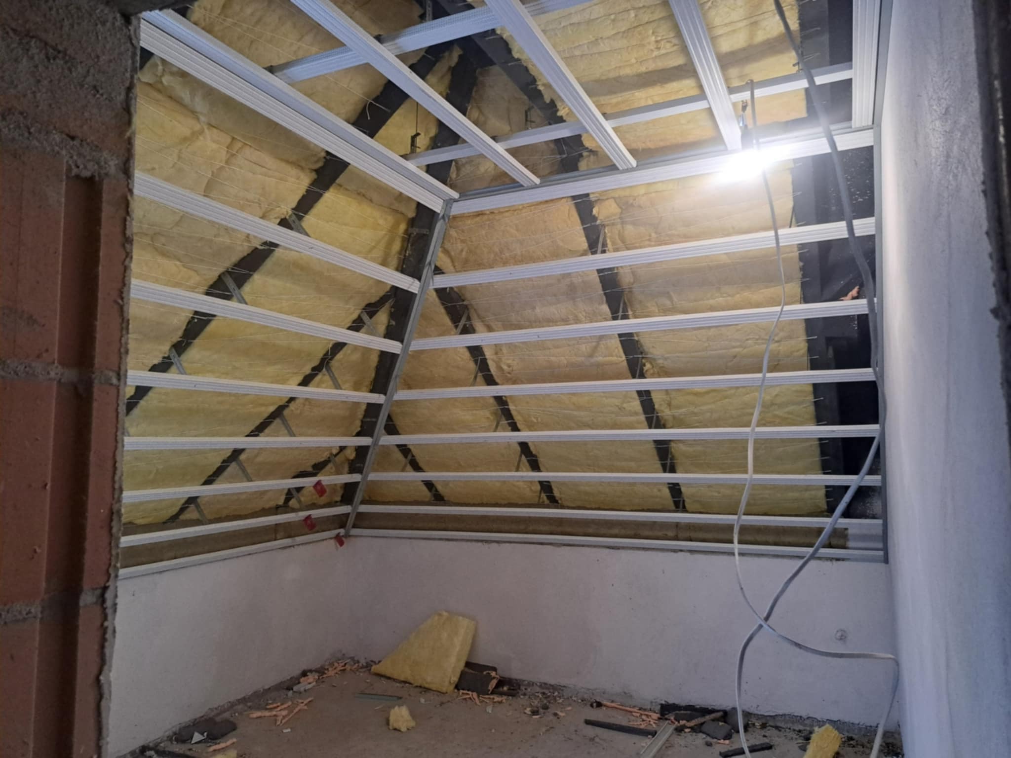 Skośne poddasze z izolacją z wełny mineralnej i metalowym stelażem pod płyty gipsowe, widok z dołu, surowy stan wykończenia.