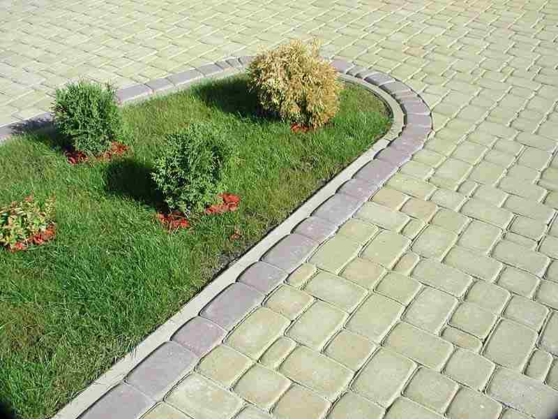 Ułożona kostka brukowa w odcieniach szarości i beżu, obrzeże z ciemniejszej kostki, trawnik z trzema krzewami i korą ozdobną.