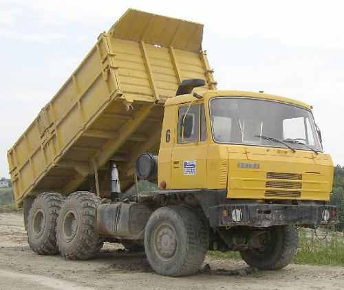 Żółta wywrotka Tatra z podniesioną skrzynią ładunkową, zaparkowana na placu budowy w Lusowie. Widoczne masywne opony i numer '6' na kabinie.